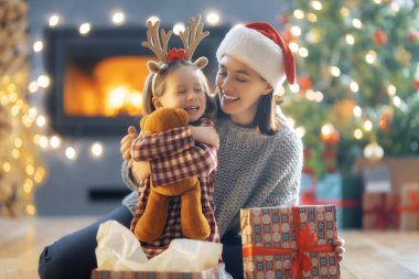 Mutlu Noeller ve mutlu tatiller. Neşeli anne ve tatlı kızı hediye değiş tokuşu yapıyor. Anne ve küçük çocuk içeride ağaçların yanında eğleniyorlar. Odasında hediyeler olan sevgi dolu bir aile.