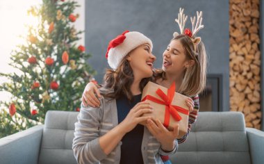 Mutlu Noeller ve mutlu tatiller. Neşeli anne ve tatlı kızı hediye değiş tokuşu yapıyor. Anne ve küçük çocuk içeride ağaçların yanında eğleniyorlar. Odasında hediyeler olan sevgi dolu bir aile.