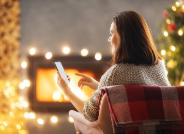 Kadın Noel ağacının yanında cep telefonu kullanıyor..