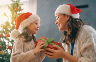Mutlu Noeller ve mutlu tatiller. Neşeli anne ve tatlı kızı hediye değiş tokuşu yapıyor. Anne ve küçük çocuk içeride ağaçların yanında eğleniyorlar. Odasında hediyeler olan sevgi dolu bir aile.