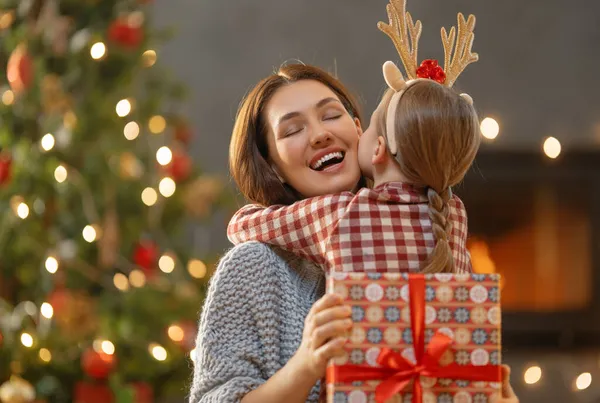 メリークリスマスとハッピーホリデー 陽気な母親とかわいい娘の女の子は贈り物を交換します 屋内で木の近くで遊んでいるお母さんと小さな子供 プレゼント付きの家族を愛する ストック写真