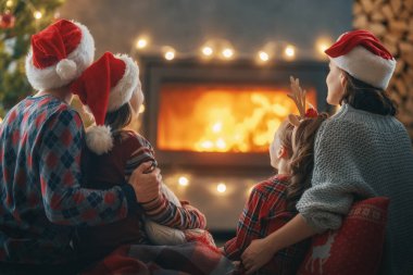 Mutlu Noeller ve mutlu tatiller. Annem, babam ve onların güzel kızları şömineye bakıyor. Ebeveynler ve çocuklar ağaçların yanında eğleniyorlar..