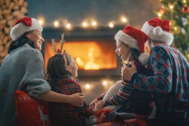 Mutlu Noeller ve mutlu tatiller. Annem, babam ve onların güzel kızları şömineye bakıyor. Ebeveynler ve çocuklar ağaçların yanında eğleniyorlar..