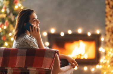 Kadın Noel ağacının yanında cep telefonu kullanıyor..