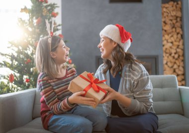 Mutlu Noeller ve mutlu tatiller. Neşeli anne ve tatlı kızı hediye değiş tokuşu yapıyor. Anne ve küçük çocuk içeride ağaçların yanında eğleniyorlar. Odasında hediyeler olan sevgi dolu bir aile.