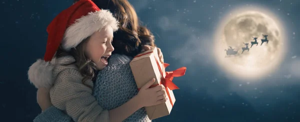 メリークリスマスと幸せな休日 お母さんとかわいい子供 サンタクロースは月の空に対して彼のそりで飛んでいます 暗い背景で休日を楽しむ家族 — ストック写真