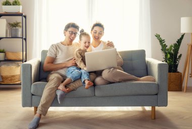 Sevgi dolu bir aile. Genç anne, baba ve kızı dizüstü bilgisayar kullanıyor. Komik anne, baba ve güzel çocuk evde kalarak eğleniyorlar..