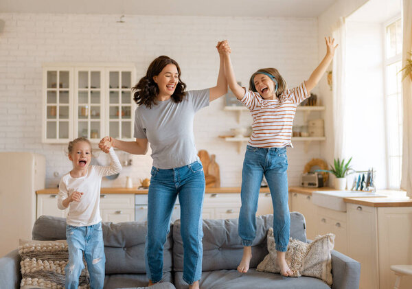 Children girls and their mother enjoying sunny morning and jumping on the sofa. Good time at home.