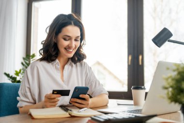 İnternetten alışveriş yapan bir kadın. Kız evde telefon ve kredi kartıyla alışveriş yapıyor..