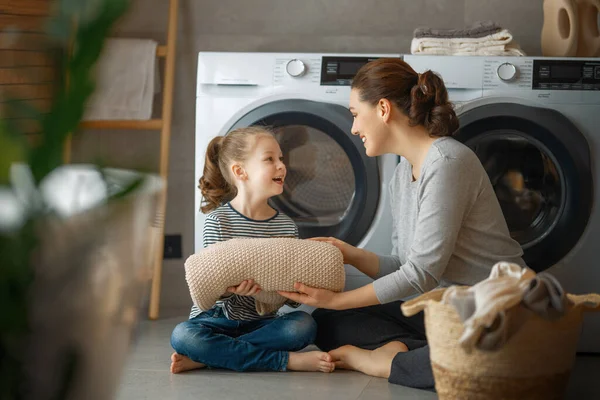 美しい若い女性と子供の女の子の小さなヘルパーは家で洗濯をしながら楽しさと笑顔を持っています — ストック写真