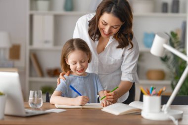 Mutlu çocuk ve yetişkin masada oturuyor. Ödev yapan ya da online eğitim alan kız.