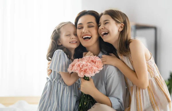幸せな日だ 子供たちの娘たちは母親を祝福し 彼女の花を与えています ママと女の子は笑って抱き合っている 家族の休日と友情 — ストック写真