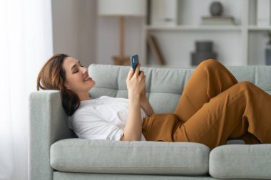 Mutlu, sıradan, güzel bir kadın evdeki kanepede oturan bir telefonu kullanıyor..
