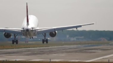 Slow motion shot of landing jet liner, rear view from end of runway. Passenger plane fly down and touch ground