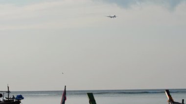 Passenger plane approaching to land at Phuket Airport. Boats sway at the shore, the plane in the background. Airliner over the sea, long shot