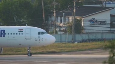 PHUKET, THAILAND - NOVEMBER 27, 2019: Side view through palm trees of Airbus A320 GoAir taxiing at Phuket airport early in the morning. Go First, GoAir Indian low cost airline. Tourism and travel