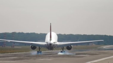 Slow motion shot of landing jet liner, rear view from end of runway. Passenger plane fly down and touch ground