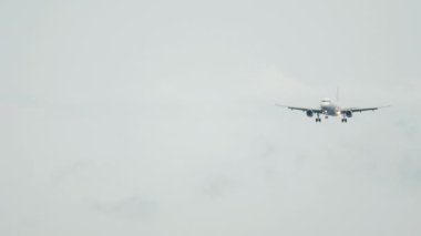 Long shot, passenger plane approaching to land. Airliner flies in cloudy gray sky, rain