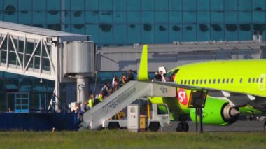 NOVOSIBIRSK, RUSSIAN FEDERATION - JUNY 12, 2022: Side view of passengers climbing a mobile ladder boarding an S7 airlines aircraft at Tolmachevo airport. Tourism and travel concept