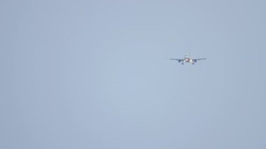 Long shot of an unrecognizable jet plane descending to land against a background of blue sky, haze
