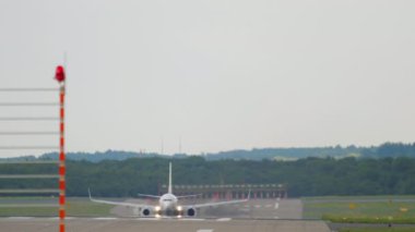 Commercial aircraft picks up speed and takes off, view from the end of the runway. Airliner flies overhead