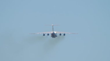 Heavy transport four-engine aircraft climb after takeoff, rear view. Multipurpose turbofan strategic aircraft