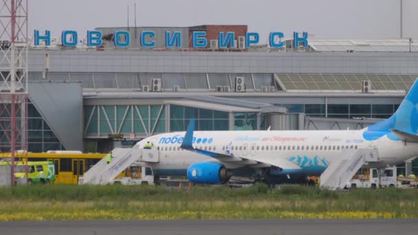 Novosiirsk ロシア連邦 2022年7月15日 トルマチェヴォ空港のターミナルでボーイング737ポベダ航空 空港の従業員は階段を飛行機に登る — ストック動画