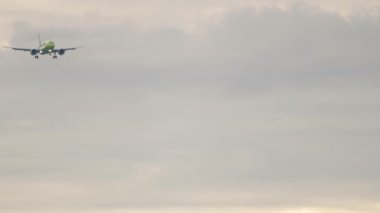 Long shot jet plane approaching to land. Silhouette of a passenger plane in a cloudy sky flying slowly. Tourism and travel concept