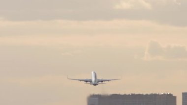 Airplane takeoff in cloudy sky. Jet plane flies away, long shot rear view. Tourism and travel concept