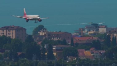 SOCHI, RUSSIA - JULY 30, 2022: Long shot, jet passenger plane Airbus A320 of Rossiya descends to land over the infrastructure of the city in Sochi International Airport. Tourism and travel concept