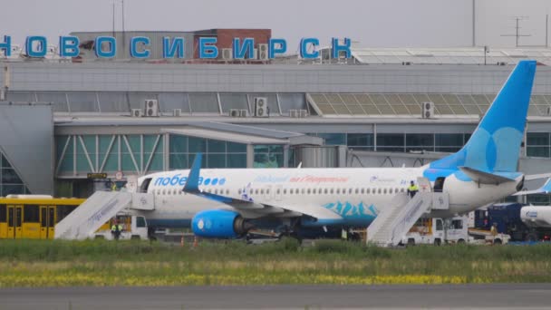 ロシア連邦のノヴォシビルスク 2022年7月15日 ポベダ航空737便がトルマチェヴォ空港に到着 空港の従業員は階段を飛行機に登る — ストック動画