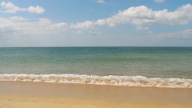 Slow motion, ocean waves roll on the sandy shore. Jet plane approaching to land over the ocean