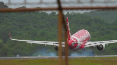 PHUKET, THAILAND - NOVEMBER 26, 2017: Low-cost airline of AirAsia landing, touching the runway and braking at Phuket airport. View of the strip through the fence. Tourism and travel concept