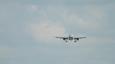 Front view of an unrecognizable commercial aircraft descending for landing. Jet plane approach. Airliner in the cloudy sky. Tourism and travel concept
