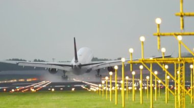 Medium shot rear view of a passenger plane arriving at the airport, landing and braking on the runway. Airfield landing strip with landing lights. Tourism and travel concept