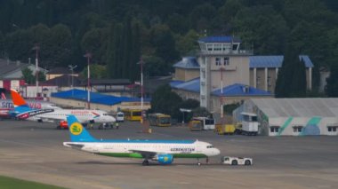 SOCHI, RUSSIA - JULY 30, 2022: Tractor towing Airbus A320-214, UK32015 of Uzbekistan Express to taxiway or runway to Sochi airport. Tourism and travel concept