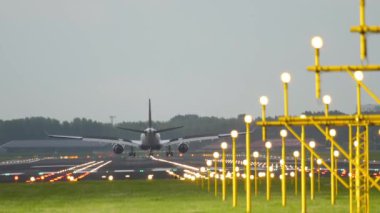 Rear view of a passenger plane landing and braking on the runway. Airfield landing strip with landing lights. Tourism and travel concept