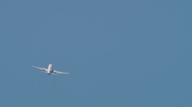 Commercial passenger airliner climbing after takeoff in the blue sky. Rear view long shot, plane turning