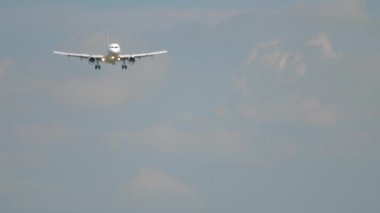 Unrecognizable aircraft approaching for landing, front view. Airliner flies on a sunny day. Tourism and travel concept