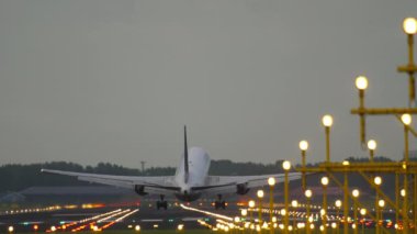 Rear view of jet airplane landing and braking. Runway brightly lit with landing lights. Tourism and travel concept