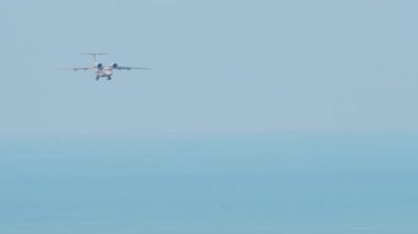Long shot plane flies over the sea, landing down. Unrecognizable airliner flies against the background of the sea. Tourism and travel concept