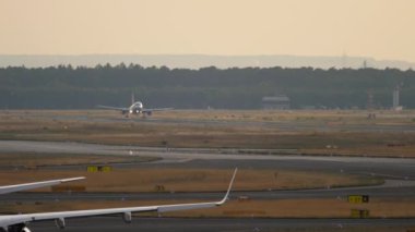 Unrecognizable passenger plane landing and braking at sunset. View of the airfield. Airliner arrival, long shot. Tourism and travel concept.
