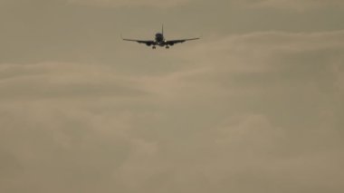 Footage of an airplane approaching to land at sunset. Airliner flight, illuminated sky background. Cinematic shot of an airplane in slow motion decline. Tourism and travel concept