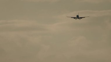 Airplane approaching to land at sunset. Airliner flight, illuminated sky background. Cinematic shot of an airplane in slow motion decline. Tourism and travel concept