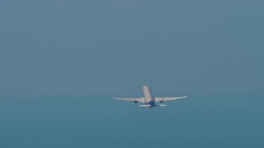 Passenger airliner climbing after takeoff in the blue sky. Rear view long shot, plane fly away