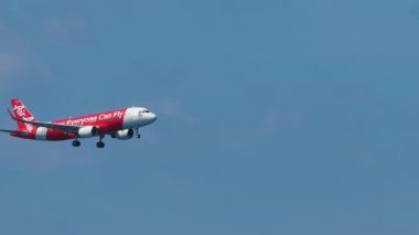 PHUKET, THAILAND - DECEMBER 01, 2018: Aircraft of AirAsia landing at Phuket airport, long shot side view. Airplane in the blue sky. Tourism and travel concept