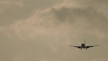 Airplane landing at sunset. Airliner flight, illuminated sky background. Cinematic shot of an airplane in the cloudy sky. Tourism and travel concept