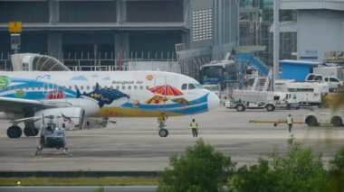 PHUKET, THAILAND - NOVEMBER 30, 2016: Airbus A320 Bangkok Air on apron of Phuket airport, side view. Tractor, ladder mobile ladder and airport workers at airfield