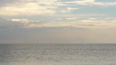Long shot, unrecognizable plane flies over the sea. Boat floating against the background of a flying airliner