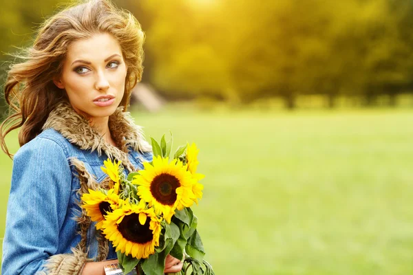 Giovane donna di moda con un mazzo di girasoli nel campo — Foto Stock